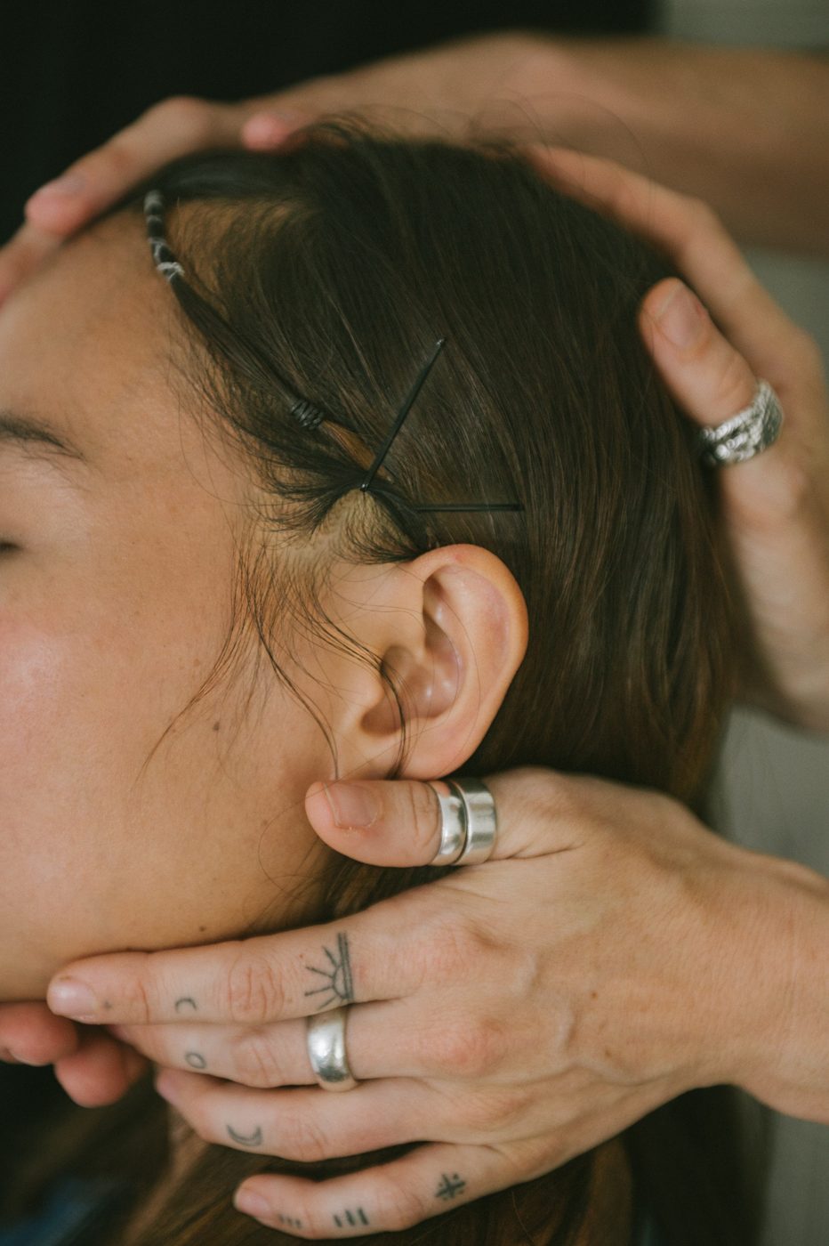 Hands with silver rings gently cradling someone's head