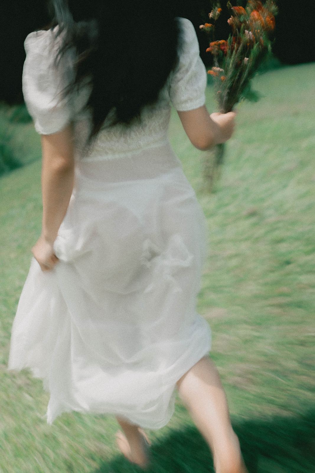 A woman in a white dress running through grass holding wildflowers