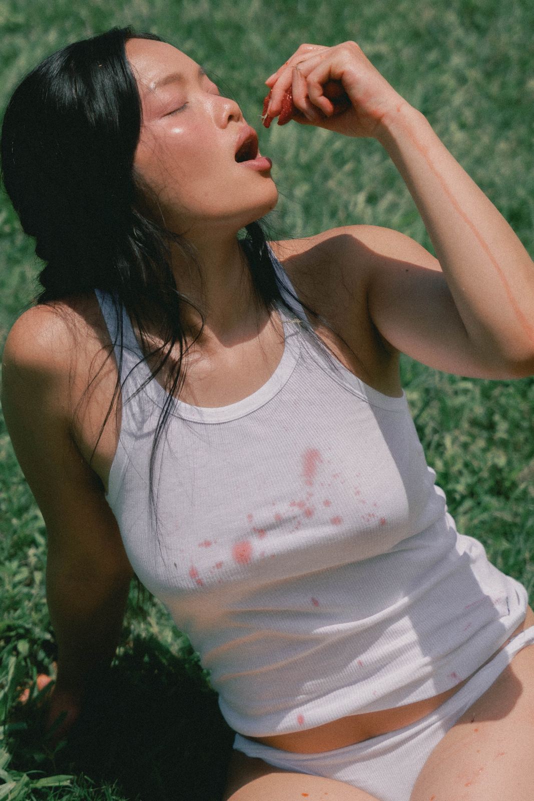 A woman in a white top lying in the grass, eating cherries