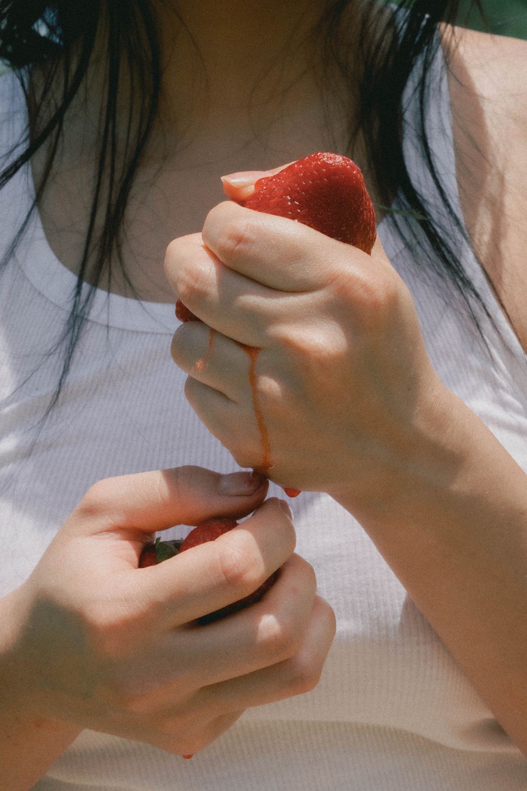 Hands holding a strawberry against a white top
