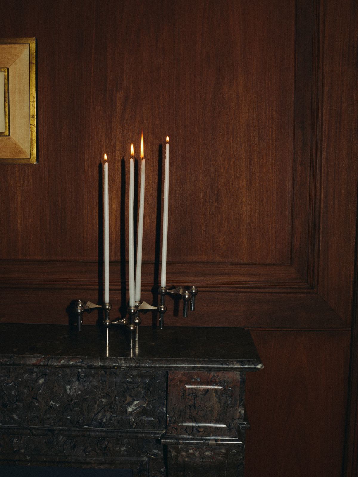 Tall candles in silver candlesticks on a marble mantelpiece